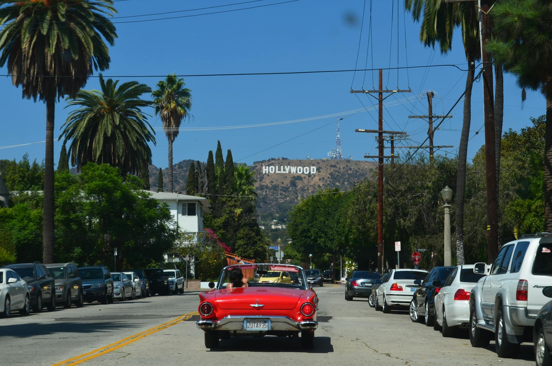 red convertible driving on los angeles street toward hollywood sign