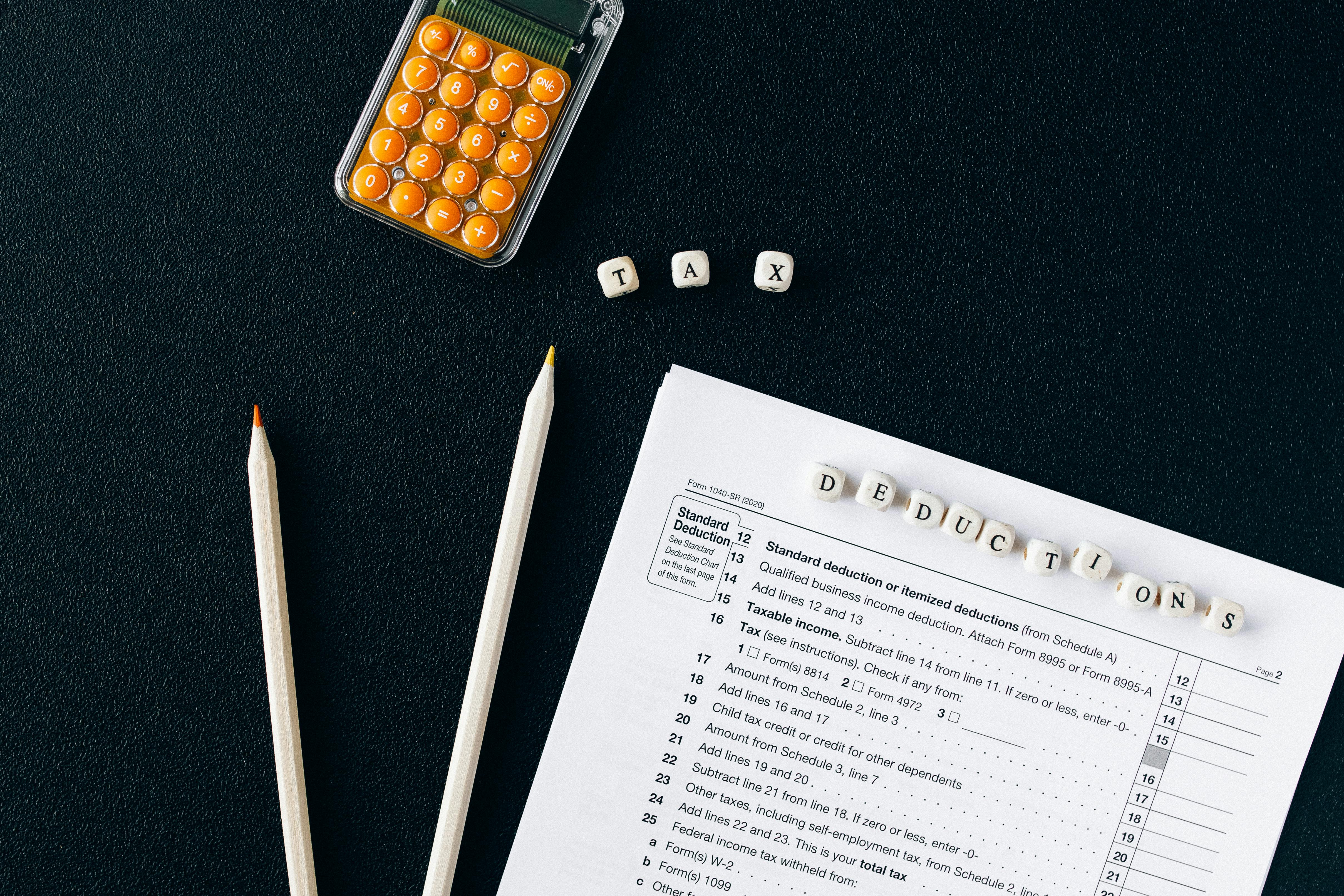 calculator, paper and pencils on a table with tax deductions spelled out in cubes